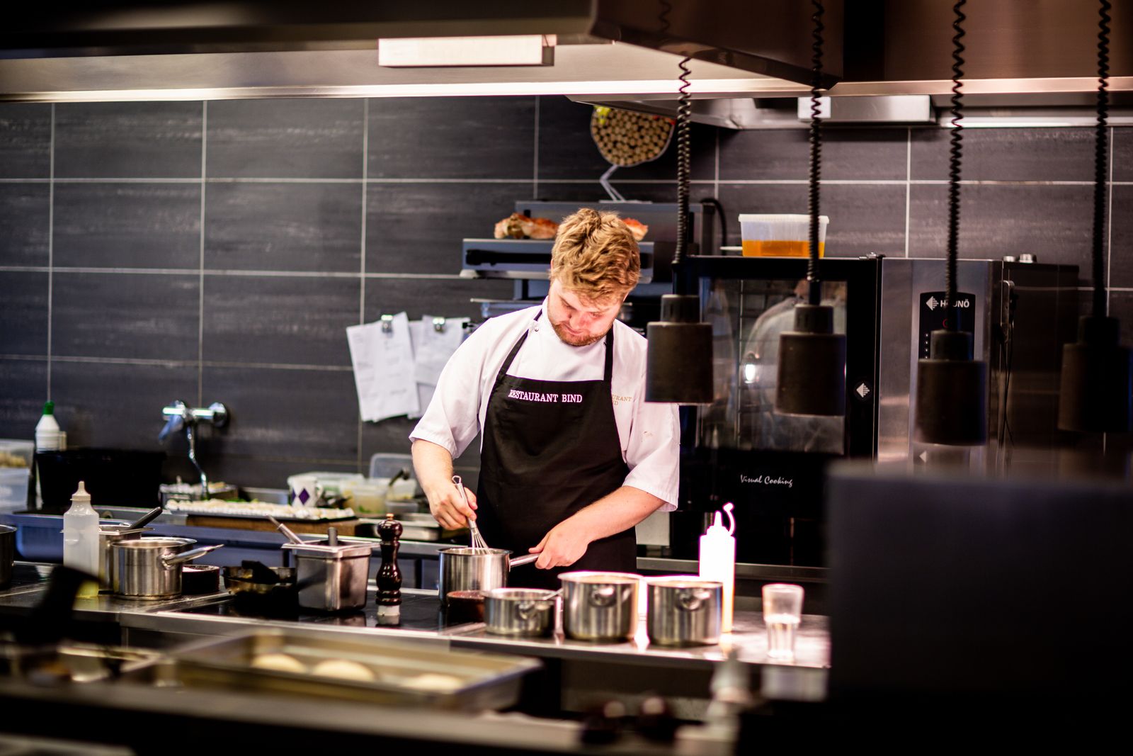 A cook working a commercial line under heat lamps and a hood, the kind of flow a restaurant kitchen layout is designed to create